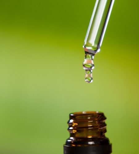 Close-up of drop of oil dripping from pipette into bottle of essential oil